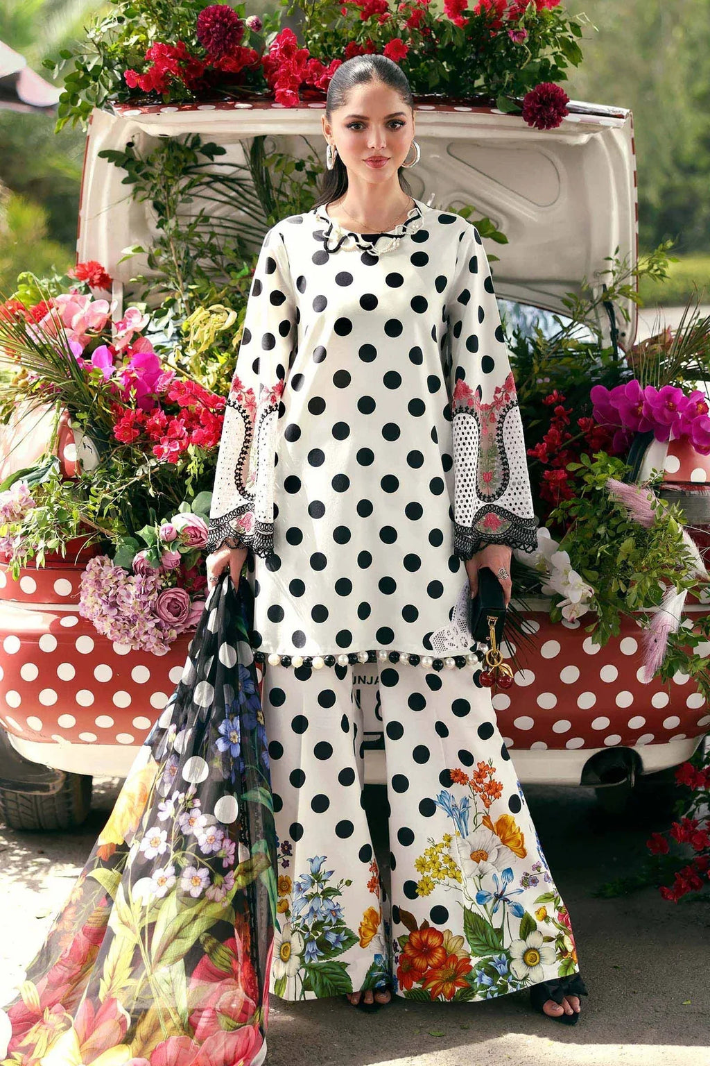 Woman in white polka dot floral print palazzo suit with matching dupatta, standing by a flower-decked vintage car.