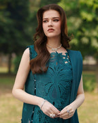 Woman in elegant teal lace dress with floral embroidery, pearl jewelry, outdoors