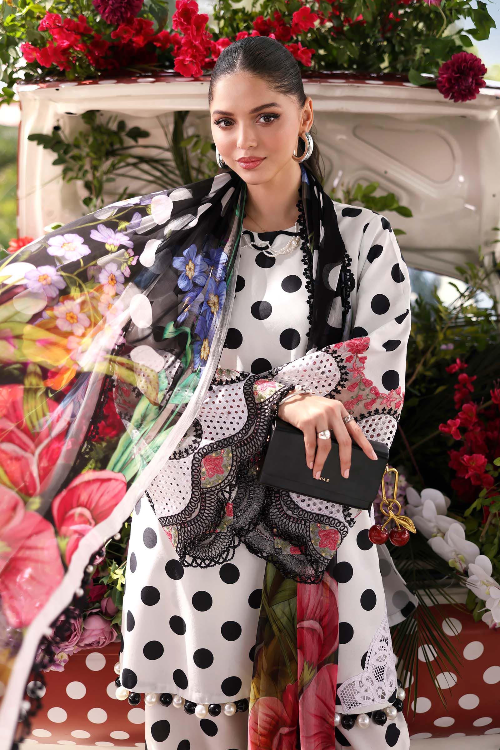 Woman in polka dot dress with floral dupatta, holding black clutch, surrounded by vibrant flowers