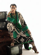 Woman in green and black printed dress with gold jewelry, posing with vintage TVs