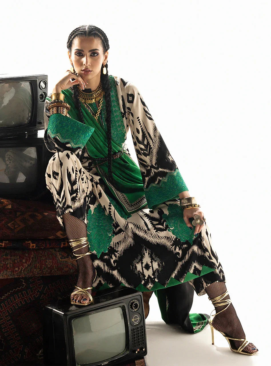Woman in green and black printed dress with gold jewelry, posing with vintage TVs