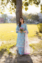 Woman in light blue floral printed kurta with pink lace, holding flowers under tree in park