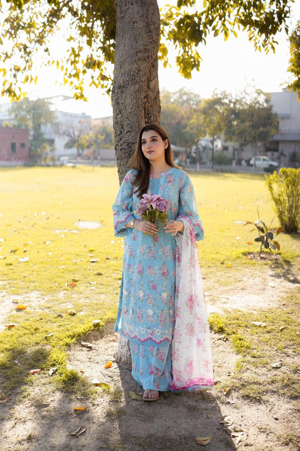 Woman in light blue floral printed kurta with pink lace, holding flowers under tree in park