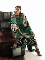 Woman in green and black patterned ethnic dress with gold jewelry, posing beside vintage TVs