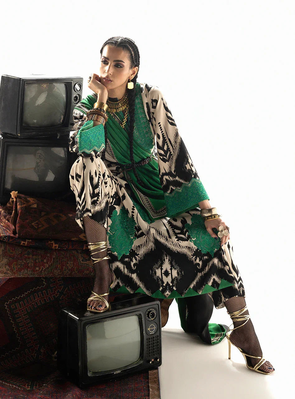Woman in green and black patterned ethnic dress with gold jewelry, posing beside vintage TVs