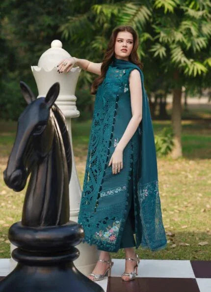 Woman in teal embroidered lawn dress with cape, posing beside giant chess pieces in garden